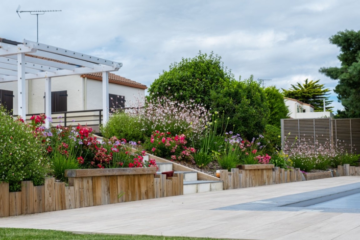 Massif fleuri avec bordure en traverses bois et bancs le long de la piscine