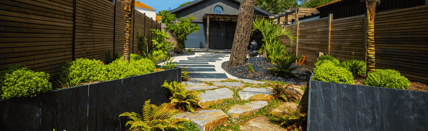 Allée de jardin en diverse matériaux : pierres naturelles, palis d'ardoise, gravillons. Entouré de plantes et d'arbres exotiques. Un jardin de reve crée par au jardin des reves.