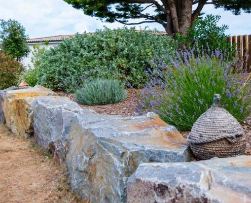 Bordure en pierres naturelles structurant un massif de lavande et d’arbustes, apportant relief et caractère au jardin.