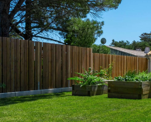 Clôture en bois ajourée avec bacs potagers sur une pelouse de jardin.