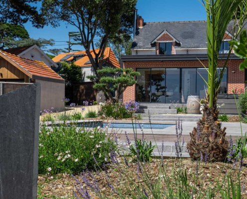 Jardin paysager contemporain aux Moutiers-en-Retz avec piscine, massifs fleuris, arbustes et palmiers, aménagement extérieur réalisé par Au Jardin des Rêves.