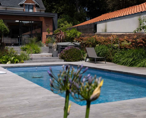 Piscine rectangulaire entourée d’une terrasse en bois et de massifs végétalisés, aménagement paysager à Pornic réalisé par Au Jardin des Rêves.