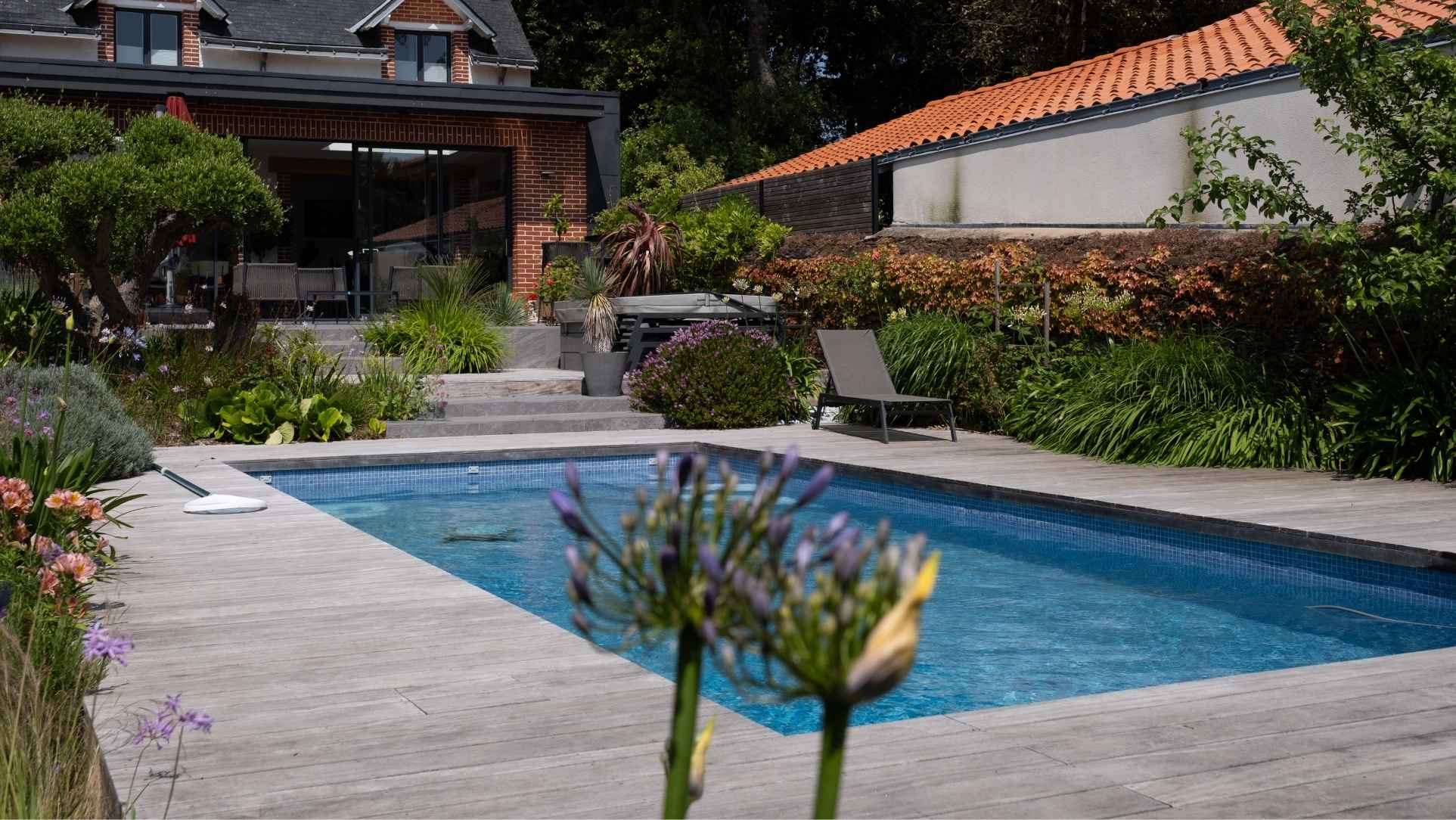 Piscine rectangulaire entourée d’une terrasse en bois et de massifs végétalisés, aménagement paysager à Pornic réalisé par Au Jardin des Rêves.