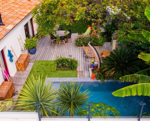 terrasse-bois-piscine-jardin-exotique-au-jardin-des-reves Vue aérienne d’une terrasse en bois à Saint-Père-en-Retz aménagée autour d’une piscine, avec végétation exotique, coins détente et mobilier extérieur, réalisation Au Jardin des Rêves.