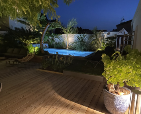 terrasse-bois-piscine-eclairage-nocturne-jardin-au-jardin-des-reves Terrasse en bois avec piscine éclairée et jardin paysager de nuit, mise en valeur par un éclairage extérieur, réalisation par Au Jardin des Rêves.