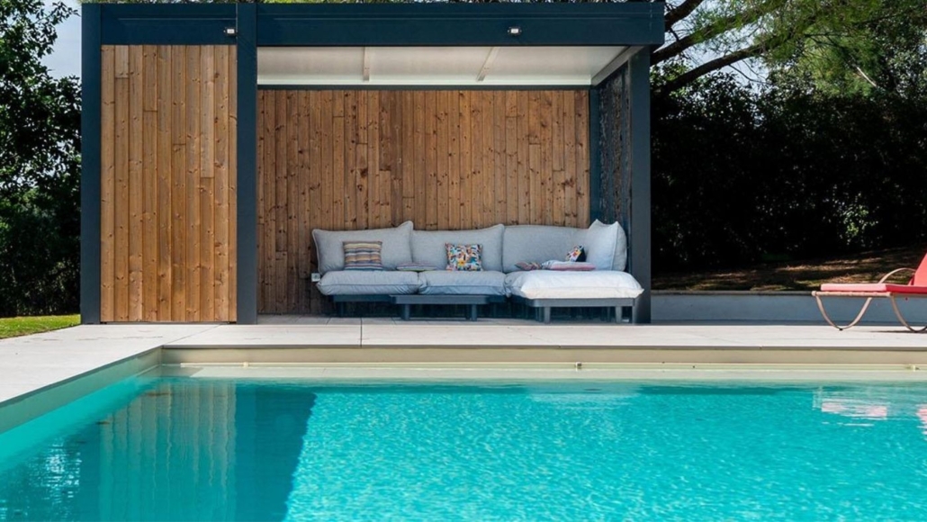 Piscine moderne avec pool house en bois et salon extérieur Piscine moderne avec pool house en bois, salon extérieur couvert et terrasse claire dans un jardin aménagé
