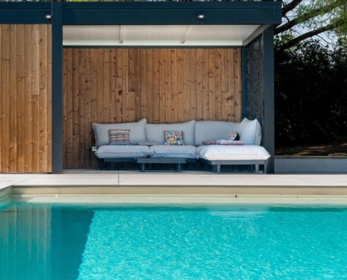 Piscine moderne avec pool house en bois, salon extérieur couvert et terrasse claire dans un jardin aménagé
