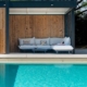 Piscine moderne avec pool house en bois, salon extérieur couvert et terrasse claire dans un jardin aménagé