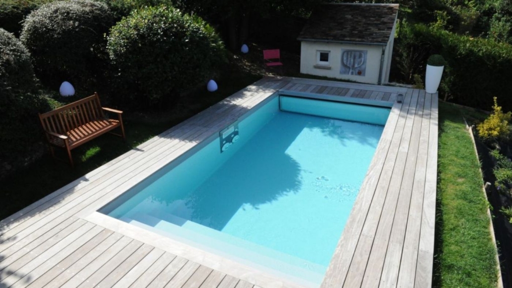 Piscine rectangulaire avec terrasse bois et jardin aménagé Piscine rectangulaire entourée d’une terrasse en bois, avec banc, pelouse et jardin paysager